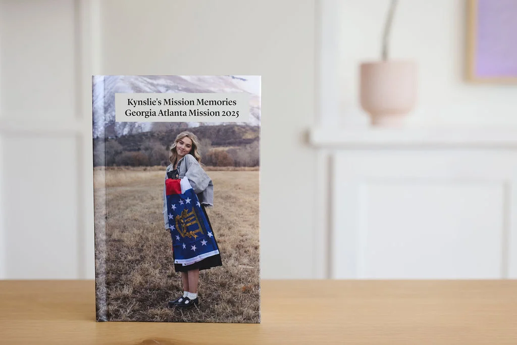 A hardbound missionary keepsake book standing upright on a wooden table, its cover featuring a photo of a missionary and a personalized title.