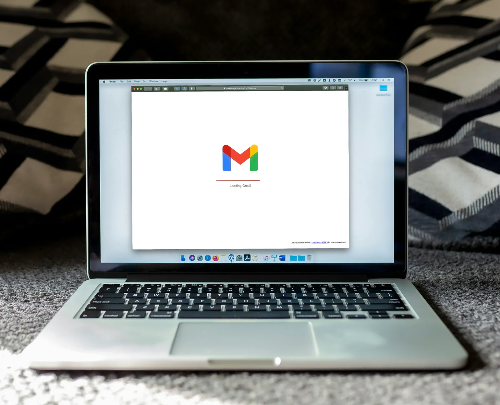 An open laptop showing a Gmail loading screen, sitting on a patterned carpet.
