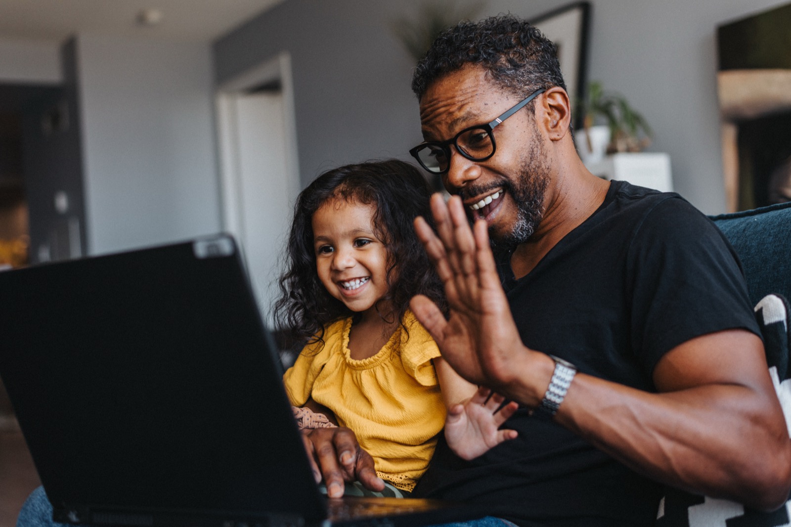 A father and young daughter video chatting on a laptop at home