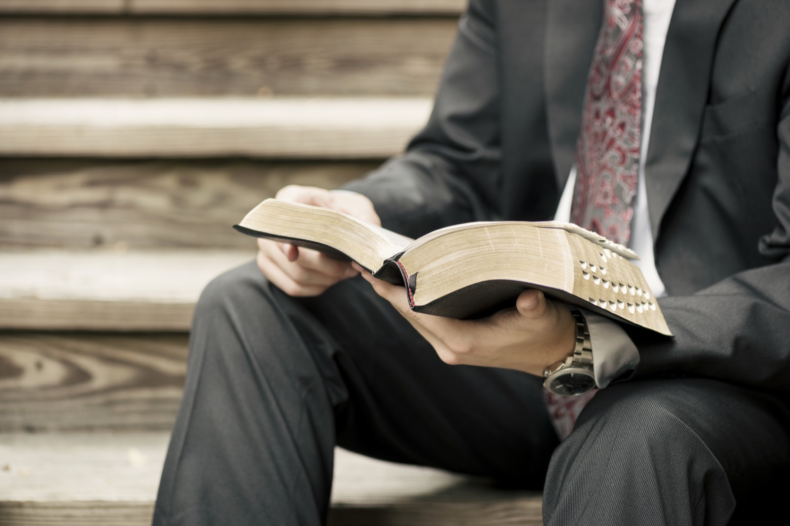 A young male missionary in a suit sitting on wooden stairs reading scriptures